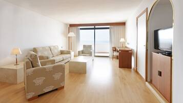 Habitación de hotel moderna con sofá, una pequeña mesa, televisor y vista al mar a través de grandes ventanales.