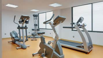 A gym with various exercise machines, including treadmills and elliptical trainers, in a well-lit room with large windows.