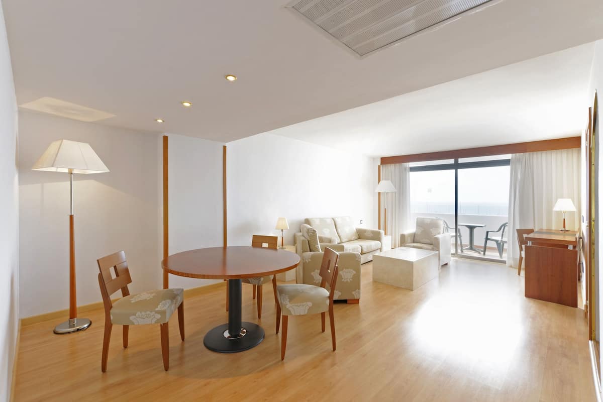 A spacious living area with a round wooden table, several chairs, a sofa, and a balcony with a view.