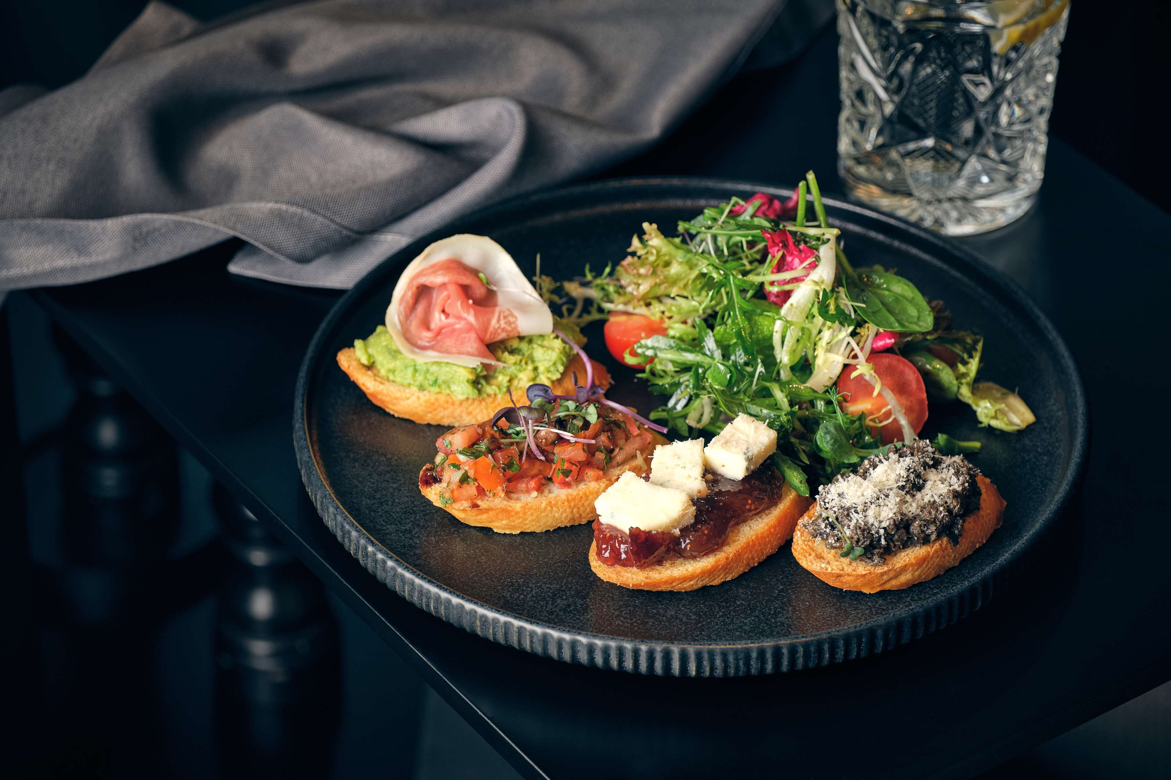 A plate with various appetizers including a salad, a sandwich with cheese, and a bruschetta with a topping.