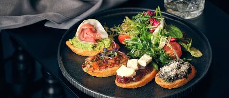 A plate with various appetizers including a salad, a sandwich with cheese, and a bruschetta with a topping.