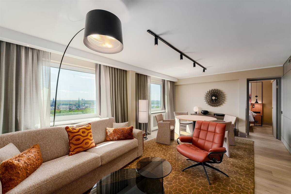 Una habitación de hotel moderna con sofá, sillón, mesa de comedor y vistas a la ciudad.