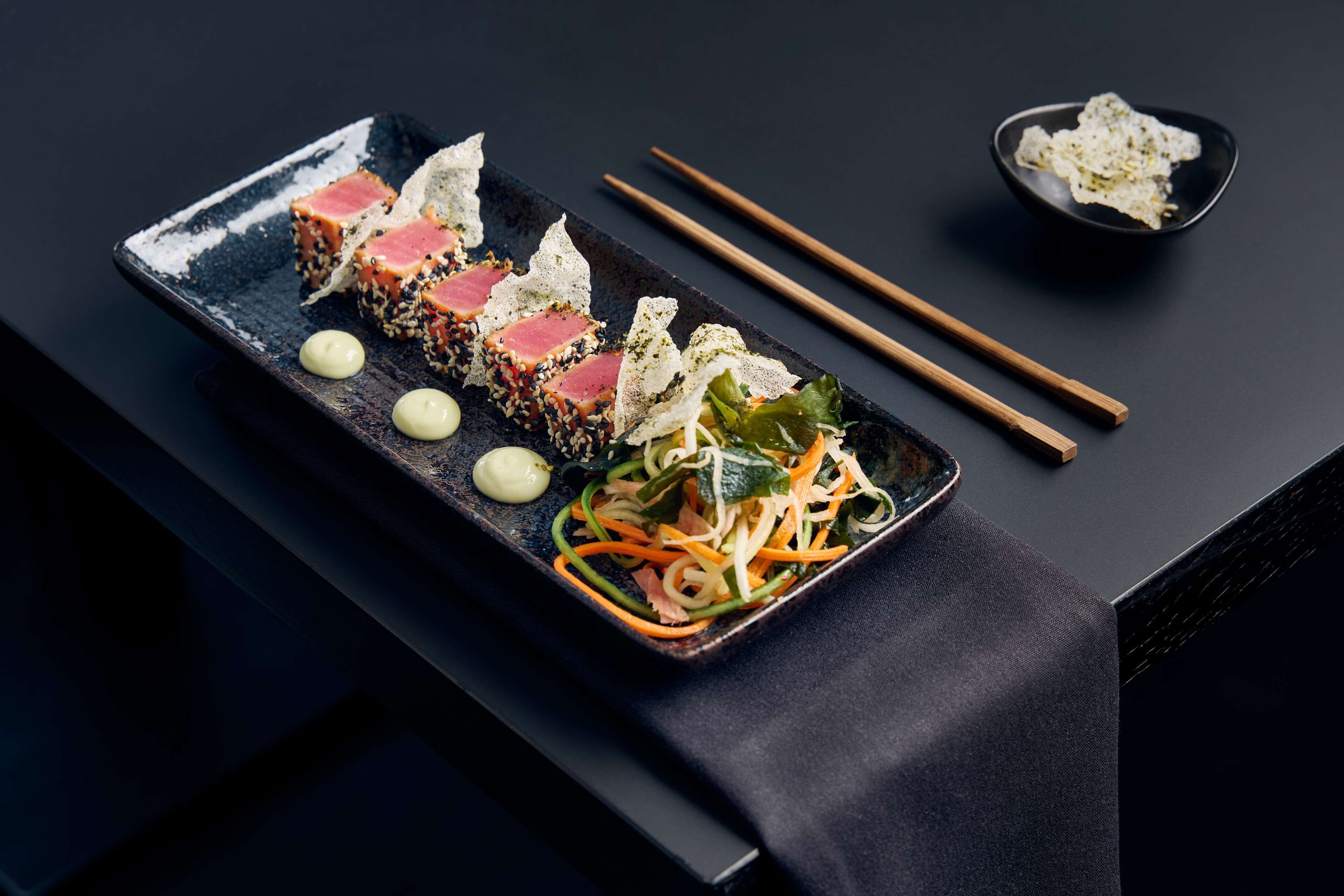 Un plato de sushi rectangular con palillos y un tazón pequeño a un lado.