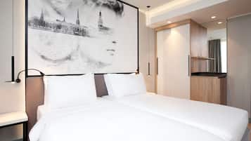 A modern hotel room with a large bed, a view of a cityscape, and a small kitchenette.