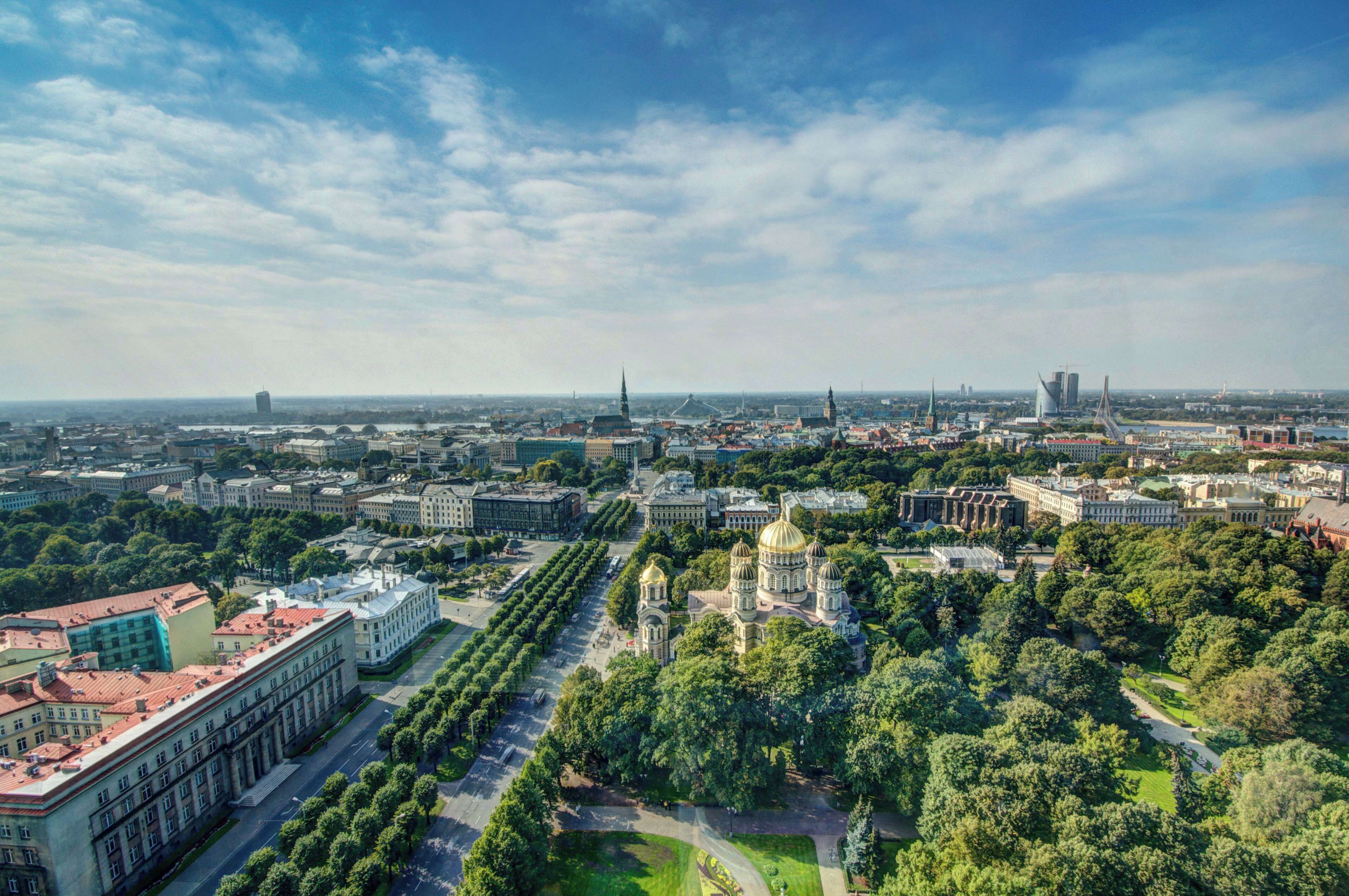 An aerial view of a cityscape with a prominent cathedral, a large building with a red roof, and a modern bridge in the distance.