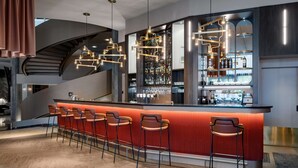 A modern bar area with a curved staircase, a bar counter with stools, and a wine rack.