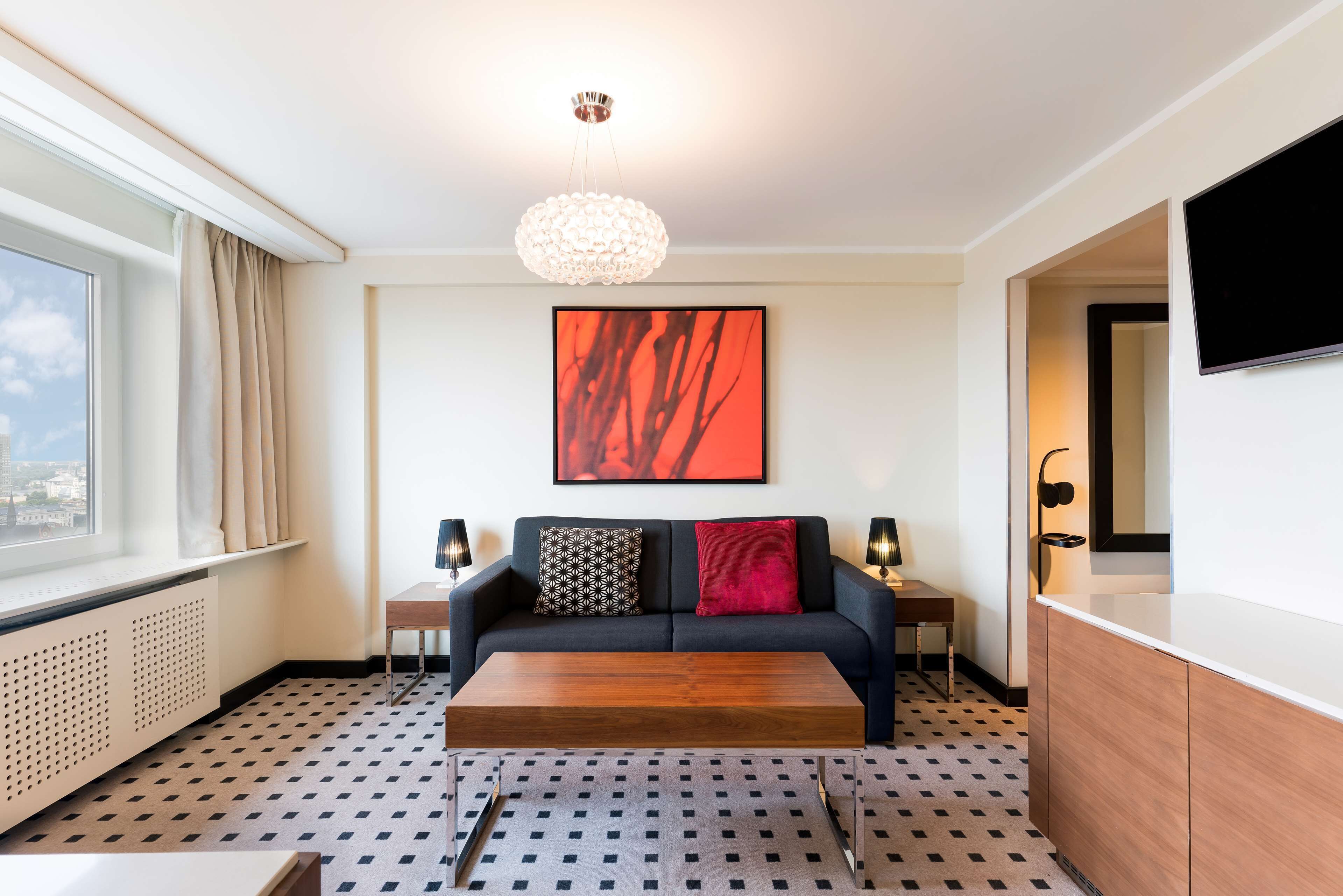 A modern living room with a sofa, a coffee table, a large abstract painting, a TV, and a patterned floor.
