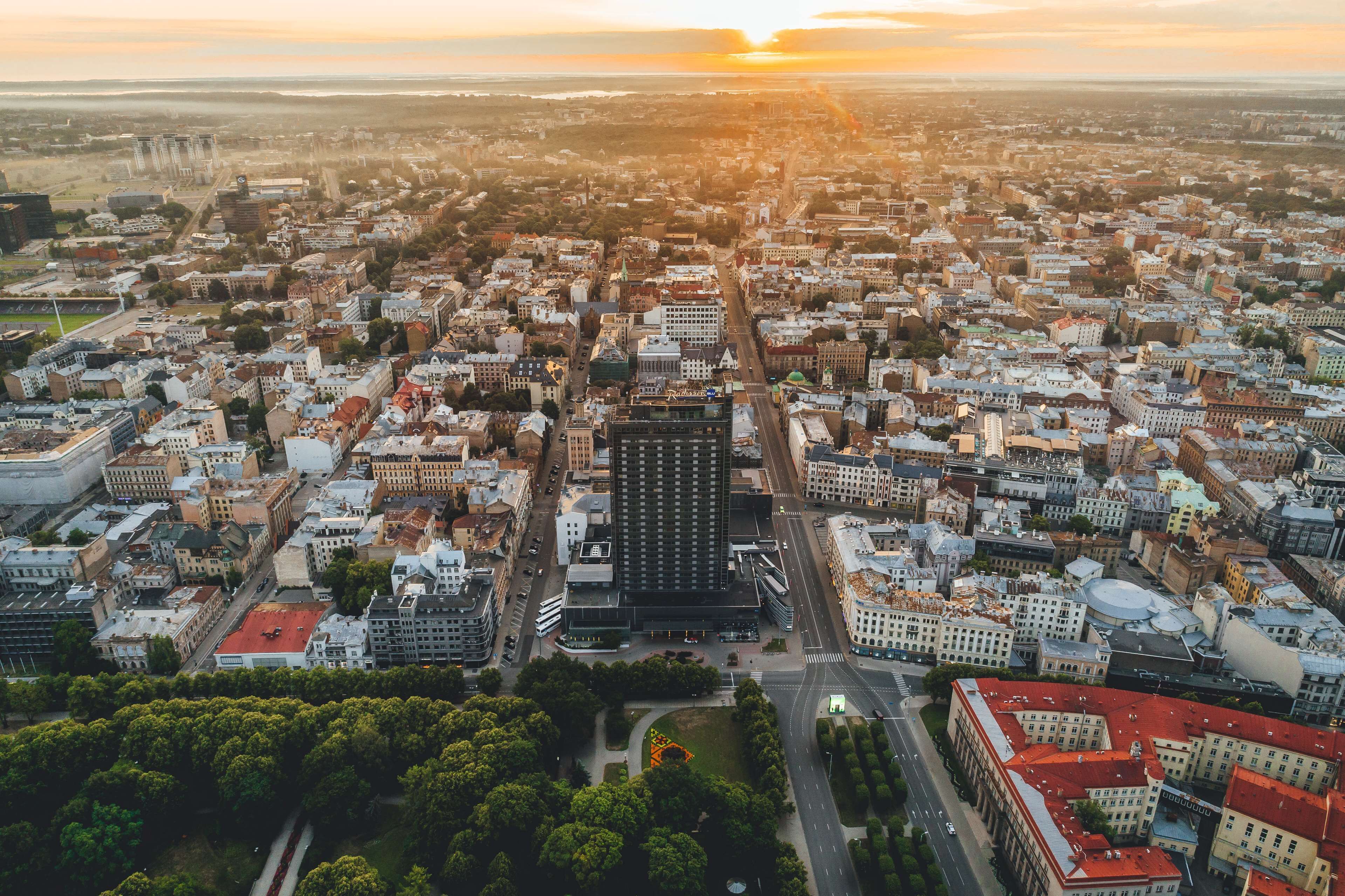 An aerial view of a cityscape with a prominent central building, surrounded by dense urban development and green spaces.