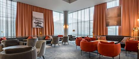 Un moderno vestíbulo de hotel con un área de estar central, ventanas amplias y obras de arte en las paredes.