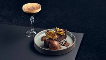 Ein Desserteller mit Schokoladendessert und einem Glas dunklem Getränk auf einem dunklen Tisch.