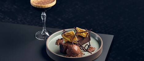Un plato de postre con un dulce de chocolate y un vaso de bebida oscura sobre una mesa oscura.