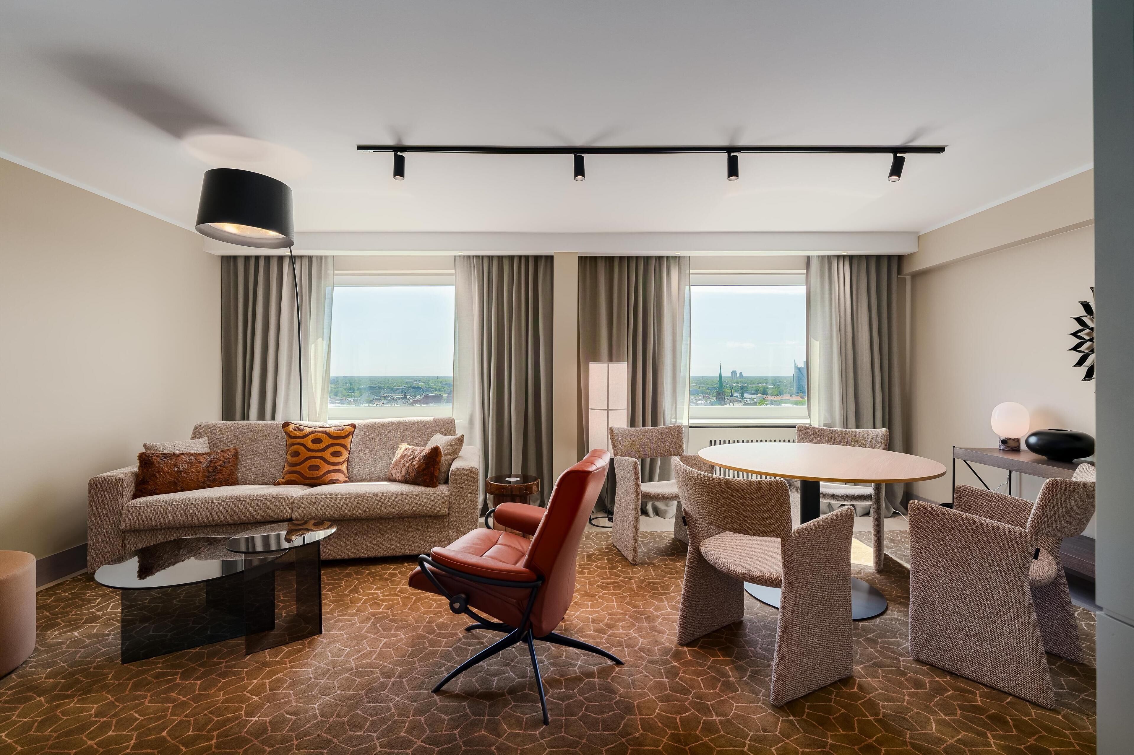 Una habitación de hotel moderna con sofá, sillón, mesa de comedor y sillas.