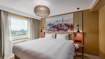 Ein Hotelzimmer mit einem großen Bett, einem Stadtbild an der Wand, Blick auf die Stadt durch das Fenster und einem modernen Kronleuchter.