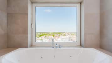 Ein modernes Badezimmer mit einer großen Badewanne, einem Fenster mit Blick auf die Stadt und einer Duschkabine.