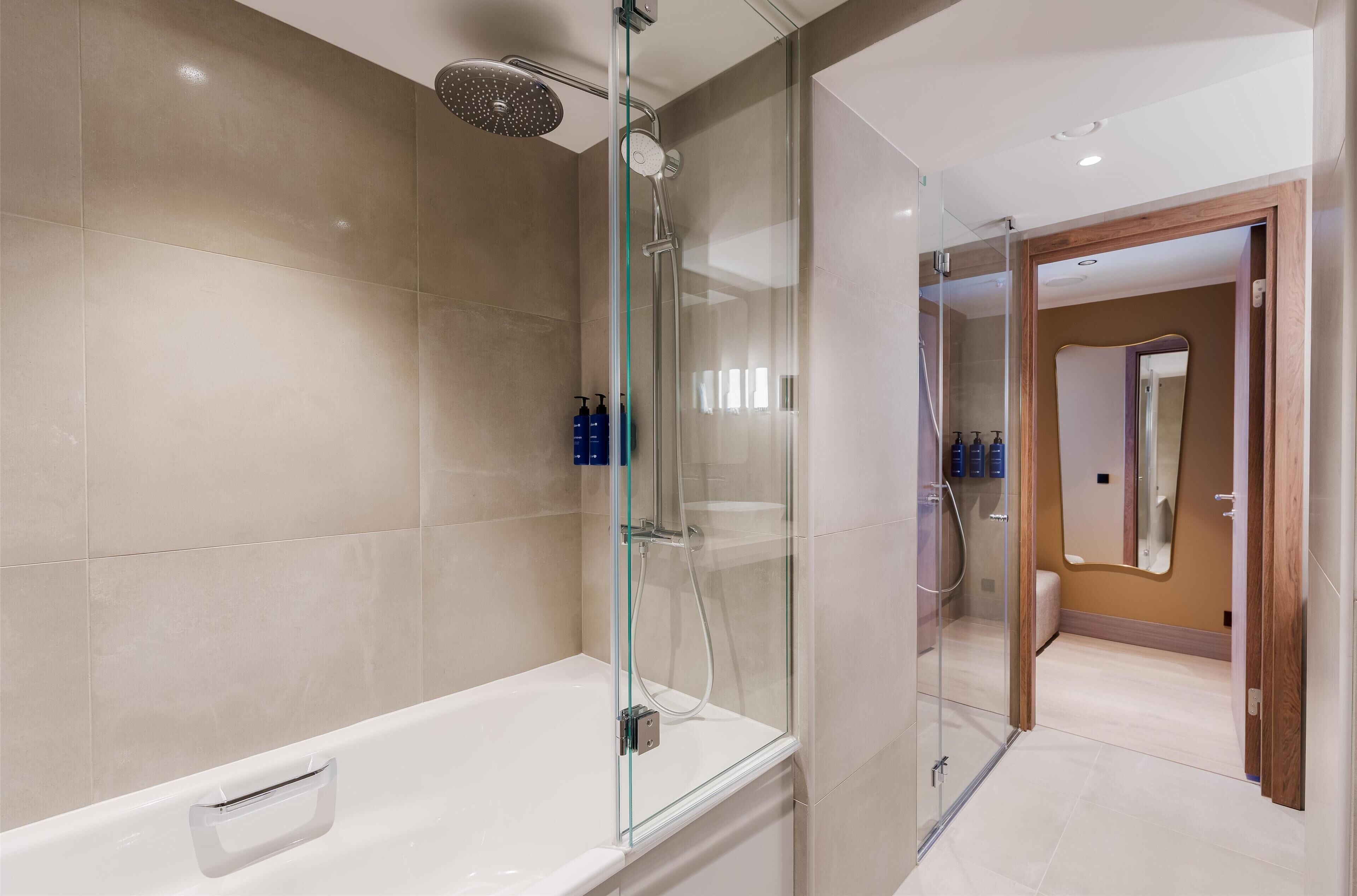 Ein modernes Badezimmer mit einer gläsernen Duschkabine, einer weißen Badewanne und einem spiegel einem Holzrahmen.