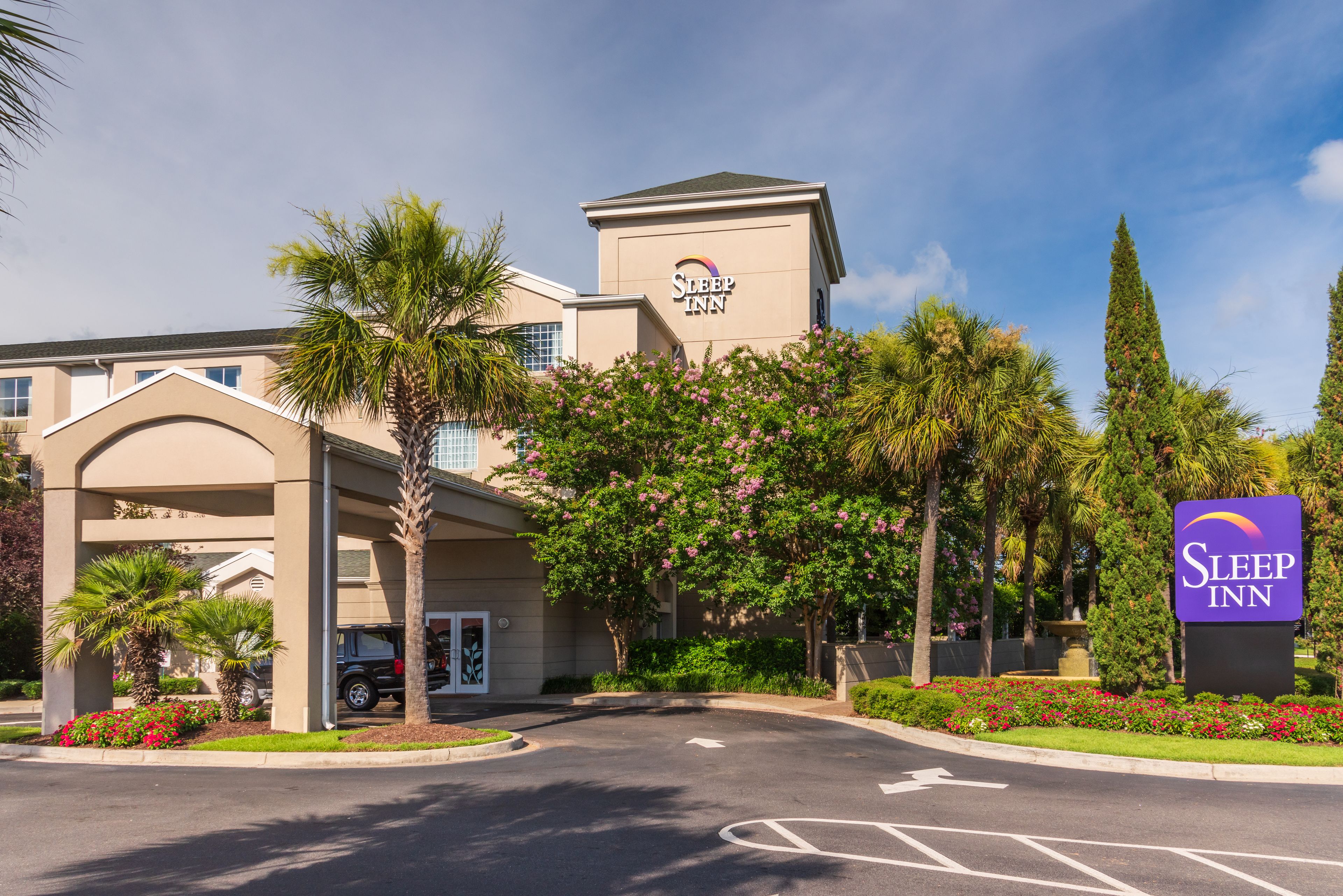 A Sleep Inn hotel entrance with a clear driveway, palm trees, and a signboard.