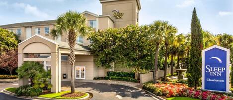 Edificio de Sleep Inn Charleston con entrada central, palmeras y jardín ajardinado.