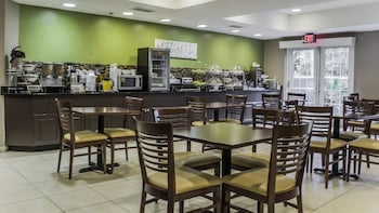 A reception area with a wooden floor, a reception desk, a sofa, a staircase, and a potted plant. at Sleep Inn Charleston - West Ashley