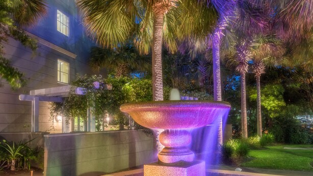 A nighttime outdoor scene with a water fountain, palm trees, and a building with illuminated windows. - Sleep Inn Charleston - West Ashley (Charleston)