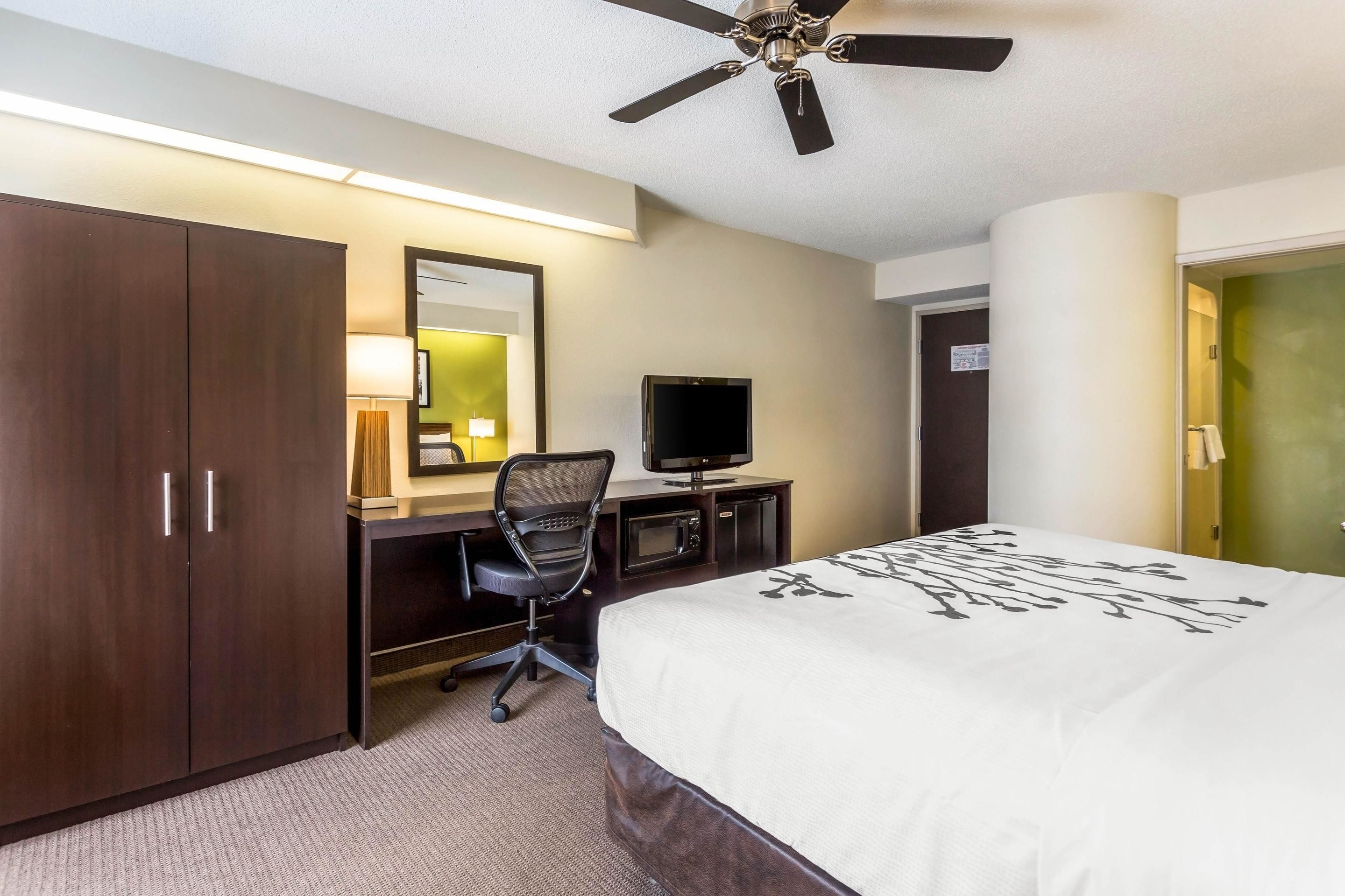 A hotel room with a bed, a desk with a chair, a television, and a wardrobe.