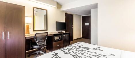 Habitación de hotel con cama, escritorio con computadora, televisión, armario y ventilador de techo.