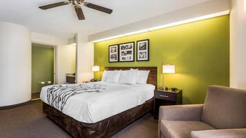 A hotel room with a bed, a chair, a nightstand, a lamp, and a ceiling fan.