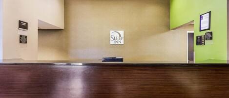 Ein Empfangsschalter mit einem "Sleep Inn" Schild, einer Holztischplatte und einer grünen Wand mit gerahmten Auszeichnungen.