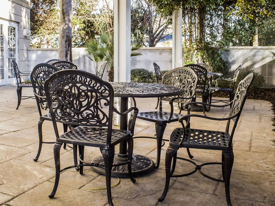 A patio area with a round metal table and chairs, surrounded by a stone floor and a white wall.