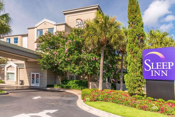 A Sleep Inn hotel with a prominent sign, surrounded by lush greenery and flowering plants. - Sleep Inn Charleston - West Ashley (Charleston)