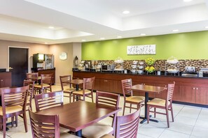 A hotel restaurant with wooden tables and chairs, a counter with food and beverages, and a green accent wall. - Sleep Inn Charleston - West Ashley (Charleston)