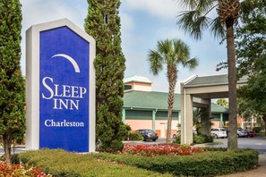 A Sleep Inn sign with a curved roof design, surrounded by well-maintained landscaping and palm trees. - Sleep Inn Charleston - West Ashley (Charleston)