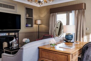 A hotel room with a TV, a sofa, a wooden desk, a mirror, a lamp, and a window with curtains.