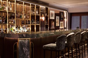 Eine Bar mit Marmorplatte und mehreren Spirituosenflaschen. Es gibt Barhocker und ein gerahmtes Bild an der Wand.