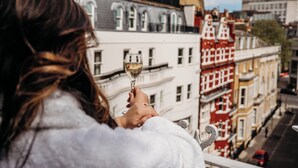 A person holding a wine glass, overlooking a row of colorful buildings. - Althoff St. James's Hotel & Club London (London)