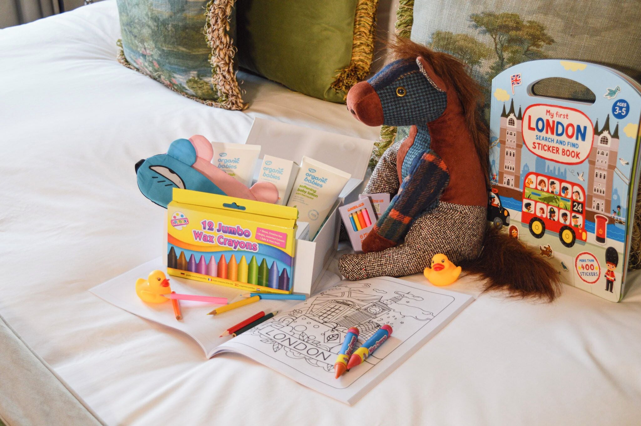 A bed with a stuffed toy, coloring materials, and a sticker book on it.