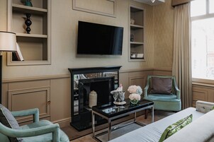 Ein Hotelzimmer mit Flachbildfernseher an der Wand, einem Kamin, einem Sofa, einem Sessel und einem Bett mit einem grünen Kopfkissen.