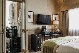 Hotelkamer met een bed, bureau met lamp, televisie, koffiezetapparaat, koffer en douche.