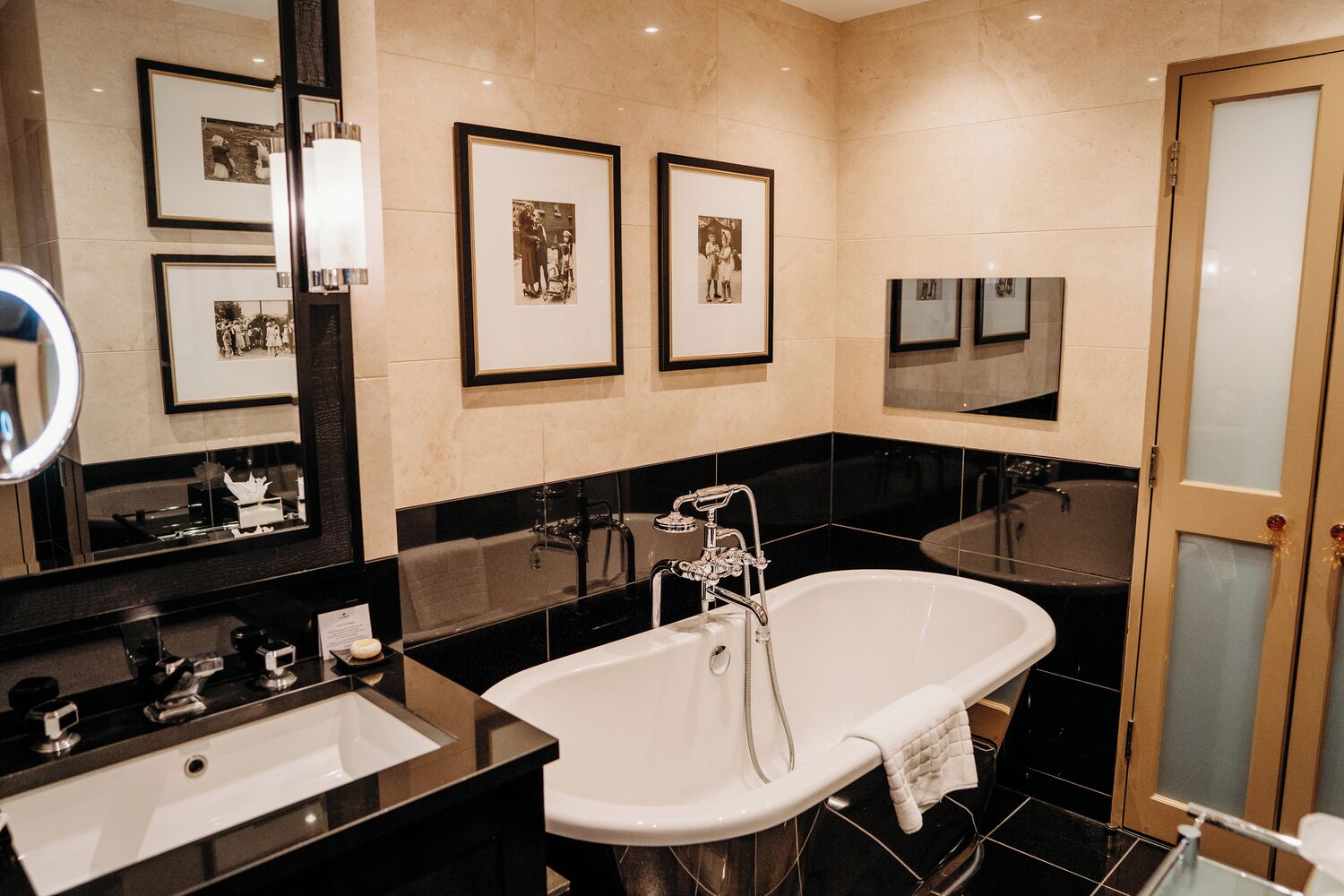 A modern bathroom with a freestanding bathtub, a large mirror, and framed photographs on the wall.