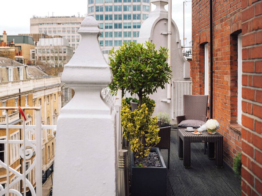 Un balcón con una maceta, una mesa con un florero y una silla.