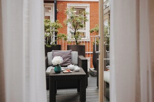 Ein Balkon mit Korbmöbeln, einem Blumentopf, einem Tisch mit Vase und Teekanne.