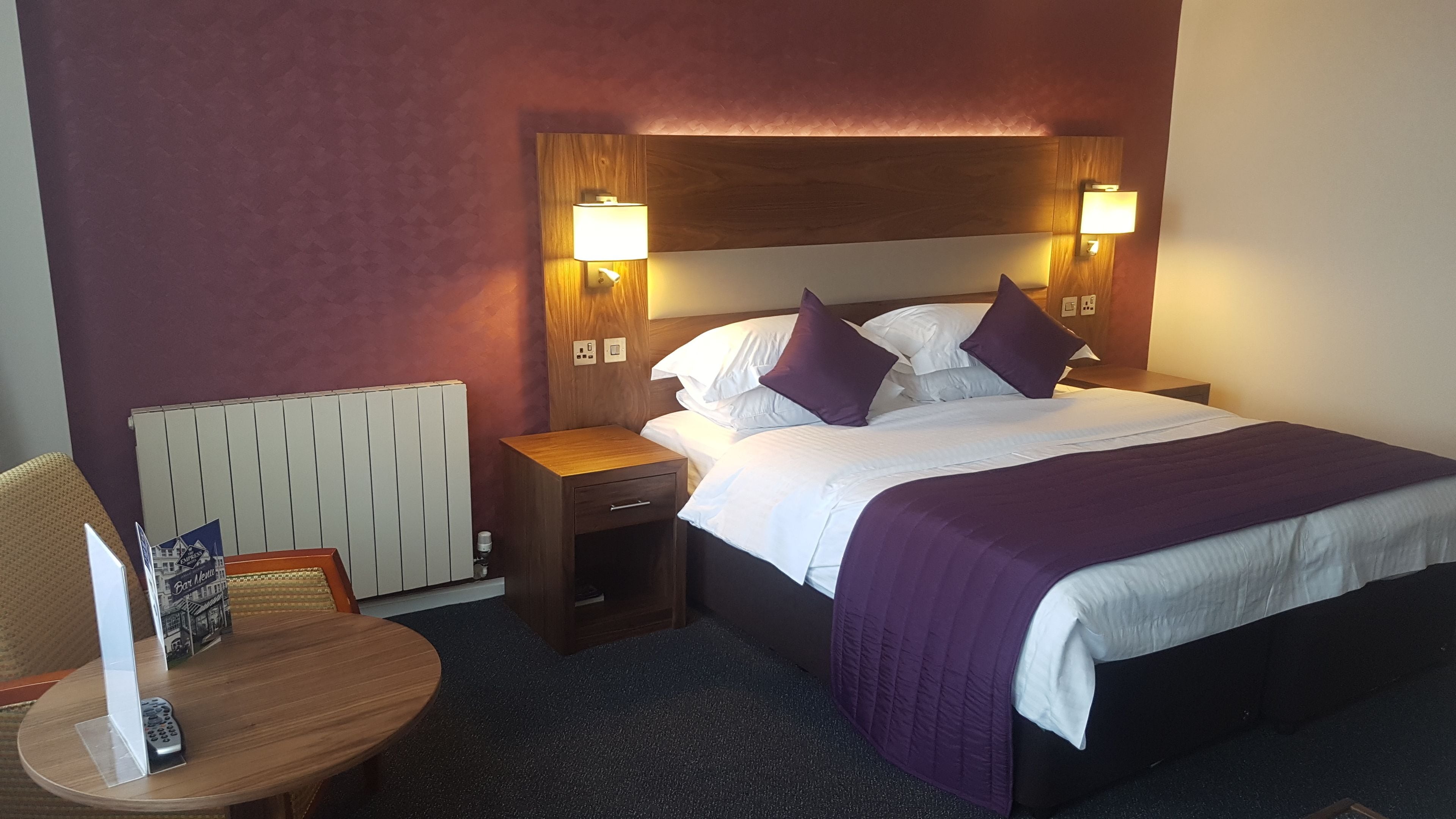 A hotel room with a bed, nightstands, a wooden headboard, and a wall-mounted lamp.