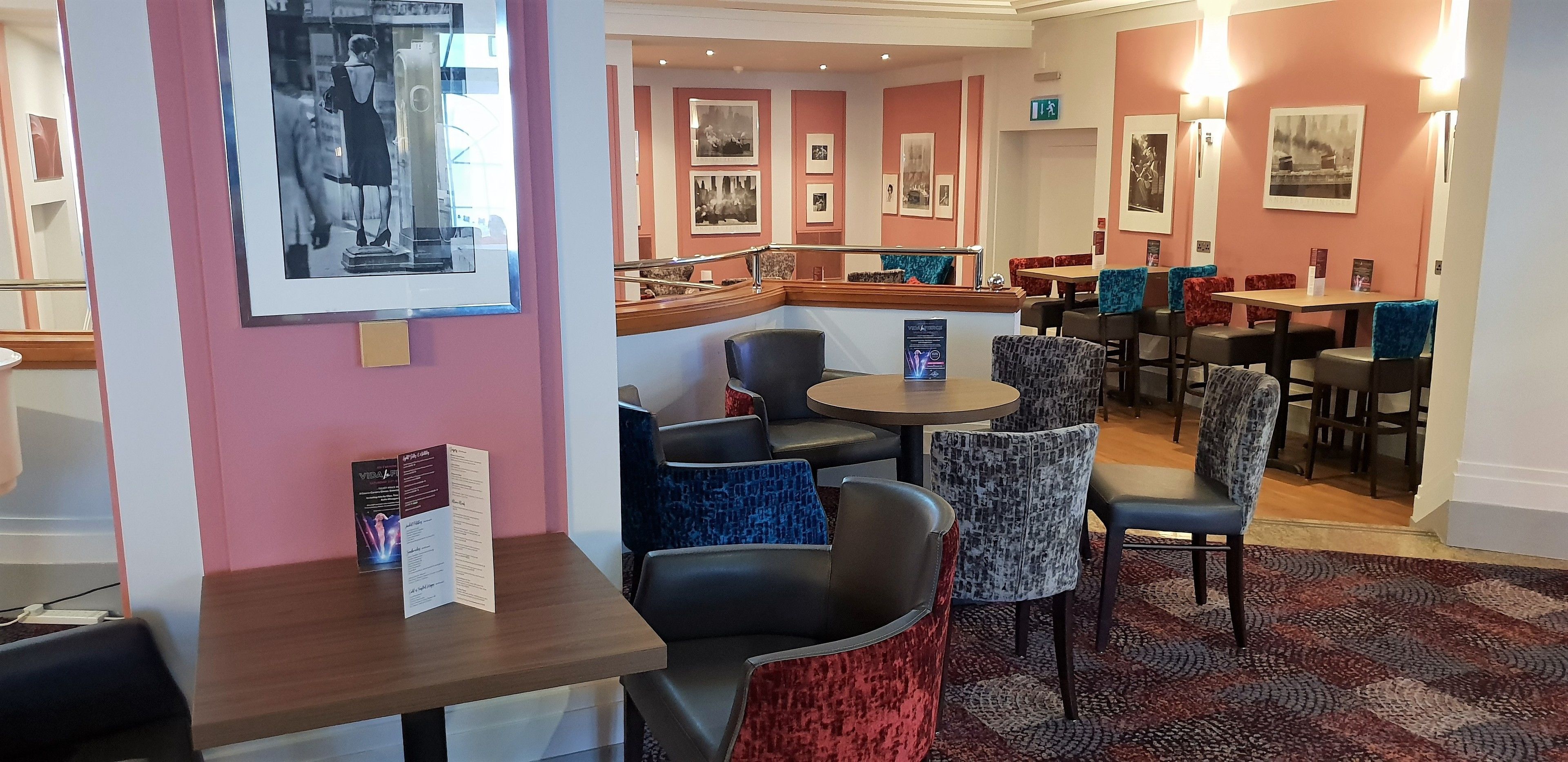 A restaurant with a pink wall, framed pictures, and a mix of red and blue chairs.