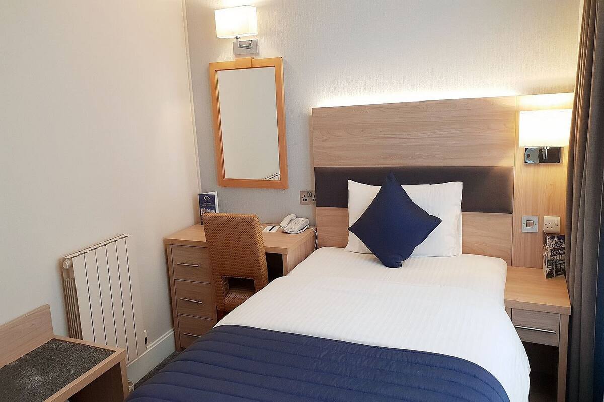 A hotel room with a bed, a desk with a chair, a telephone, and a mirror.