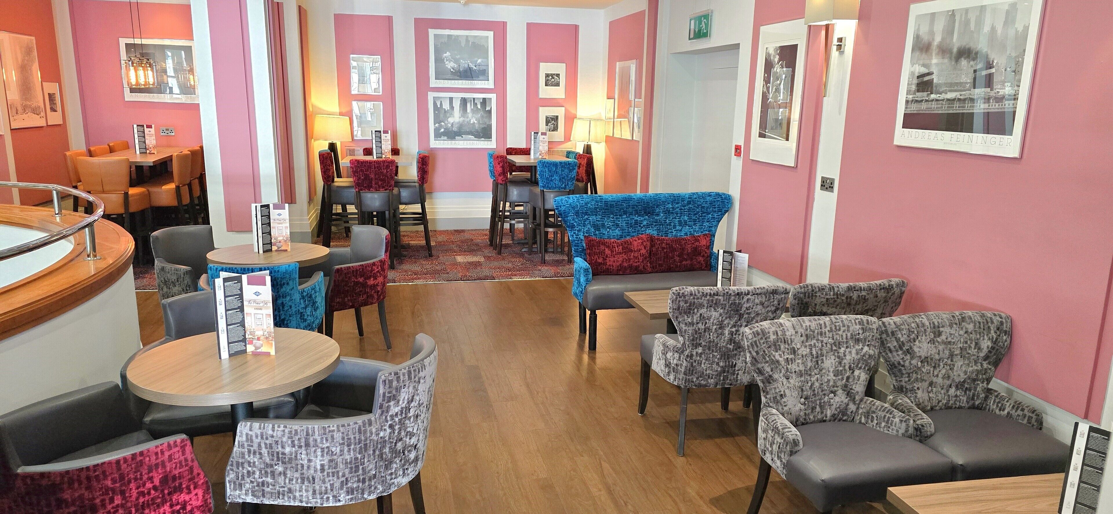 A hotel lobby with multiple seating areas, including round tables and sofas, and a bar area with a counter.