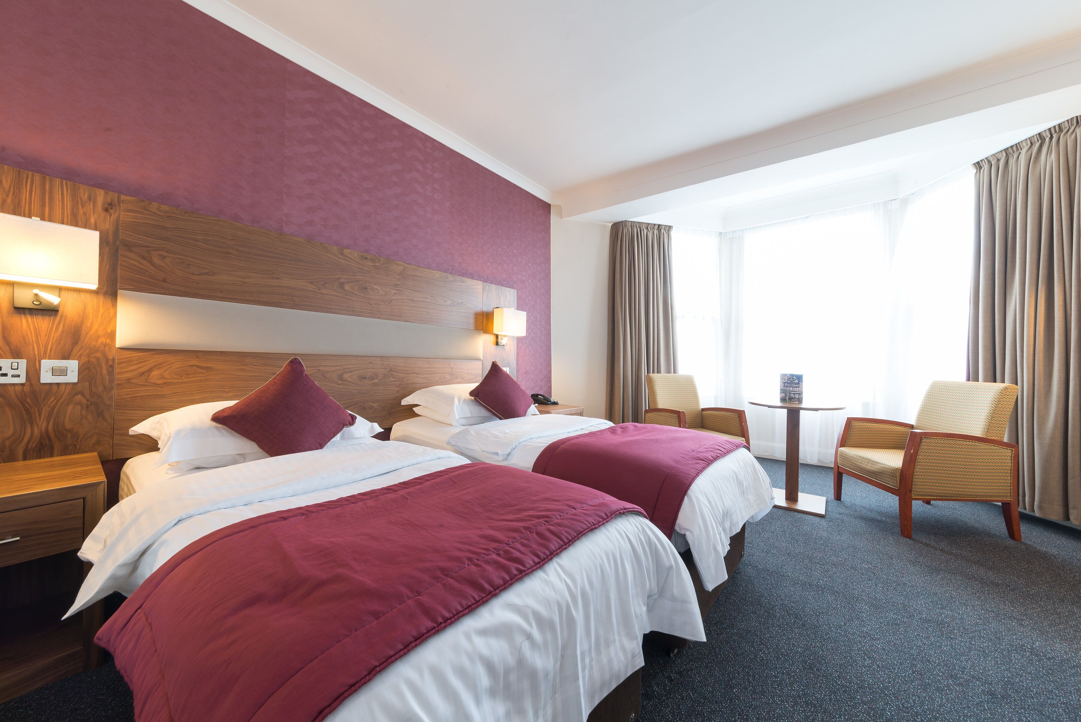 A hotel room with two beds, a small table, and a chair.