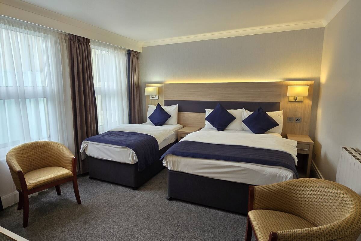 A hotel room with two beds, a desk, two chairs, and a window with curtains.