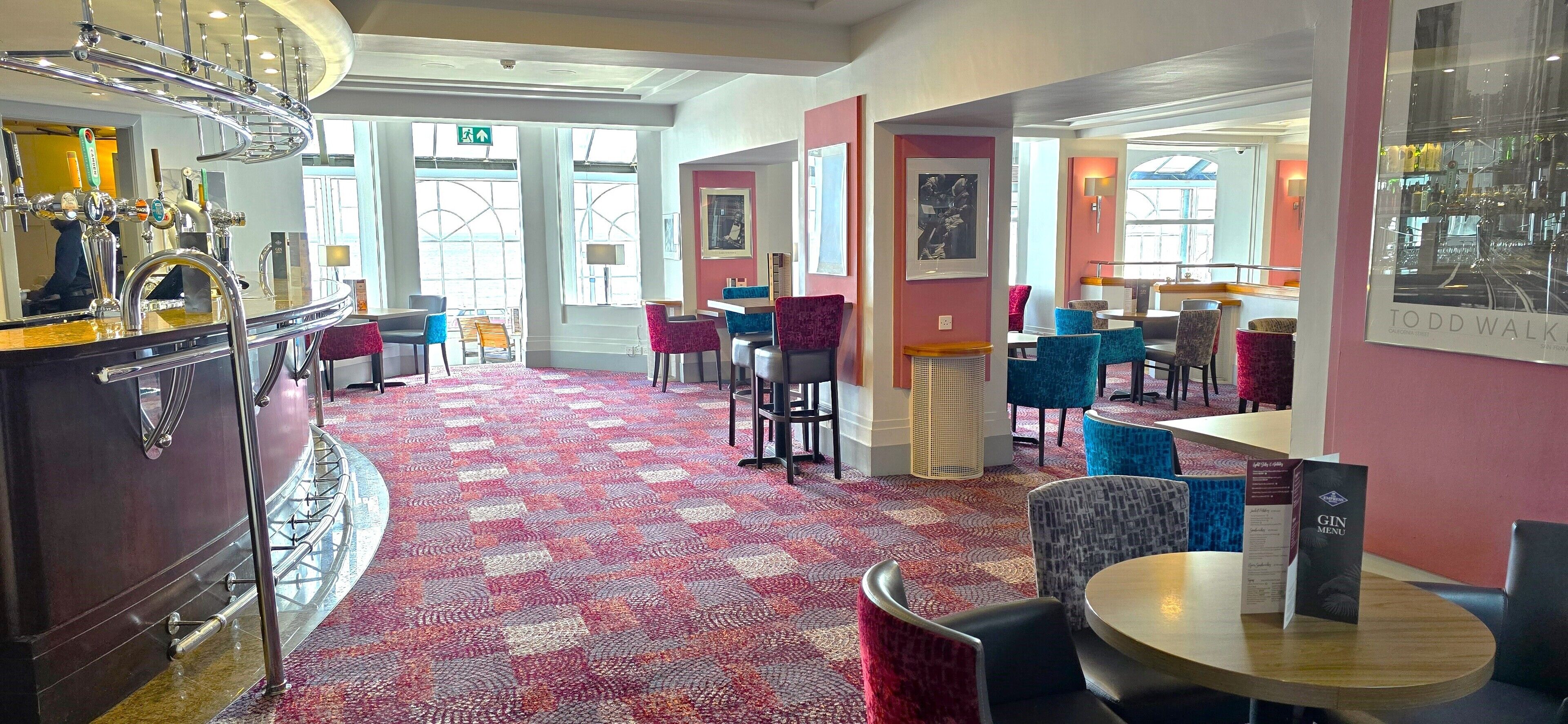 A hotel lobby with a bar area, seating arrangements, and a patterned carpet.