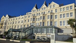 Ein mehrstöckiges Hotel im klassischen Stil, mit einem Wintergarten und einer Treppe zum Eingang.