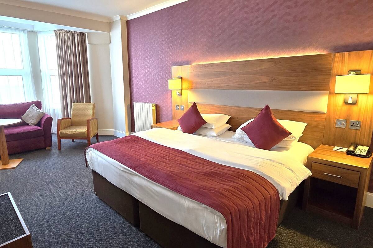 A hotel room with a large bed, two bedside tables with lamps, a chair, a small table, and a television.