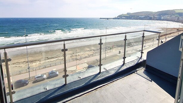 Blick auf die Küste vom Balkon mit Metallgeländer, ein Sandstrand und eine Straße mit Autos.